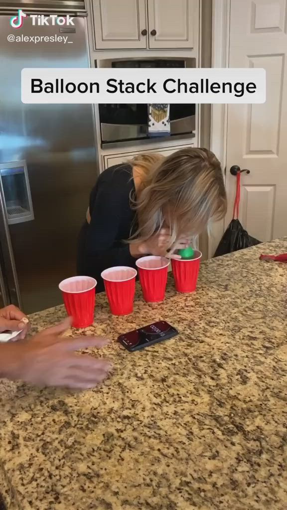 This may contain: a woman standing in front of a kitchen counter with cups on it and the words balloon stack challenge