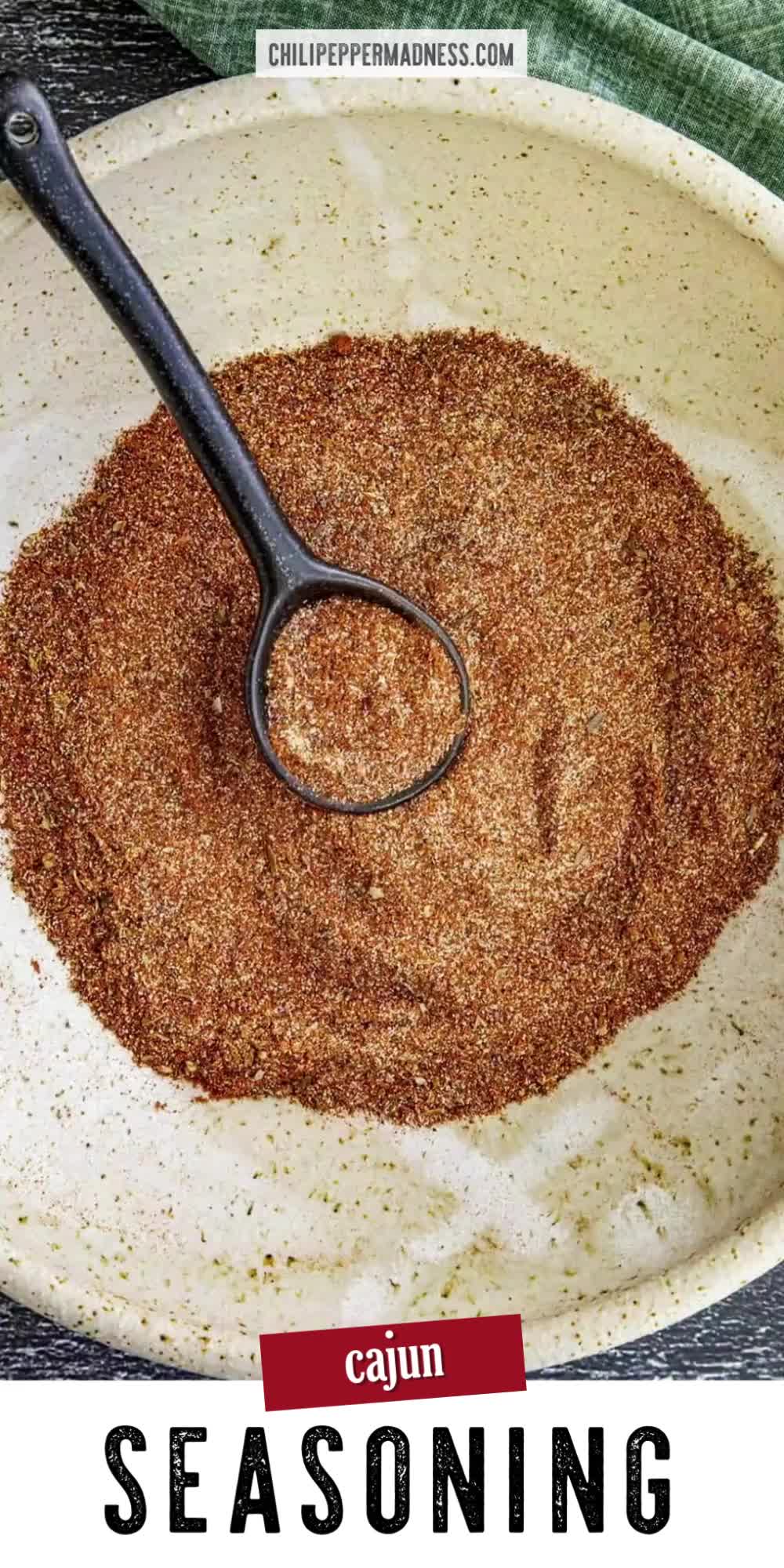 This may contain: a bowl filled with seasoning next to a spoon in the center and text reading cajun seasoning