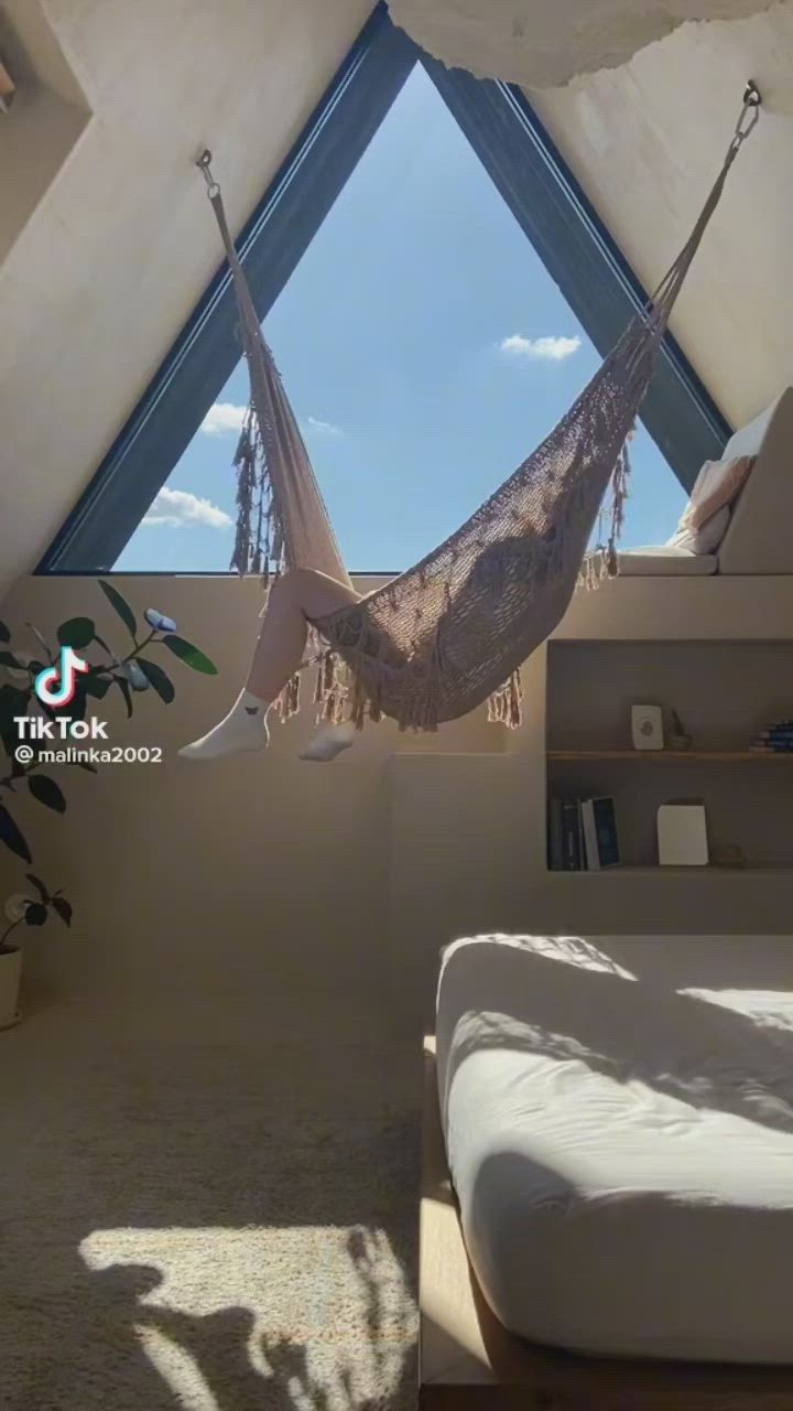 This may contain: a bedroom with a hammock hanging from the ceiling and a bed in it