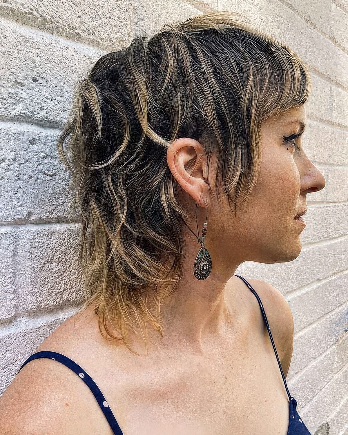 A short brunette mullet with blonde balayage and bangs plus a bit of messy texture looks all-natural.