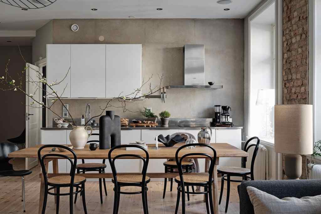 A living space with a white kitchen and exposed brick walls, wood dining table, black bentwood chairs, beige limewash wall