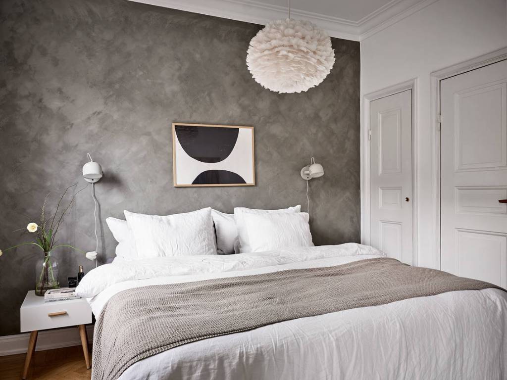 Grey limewashed walls in a bedroom with white bedding, a white area rug and white lighting fixtures