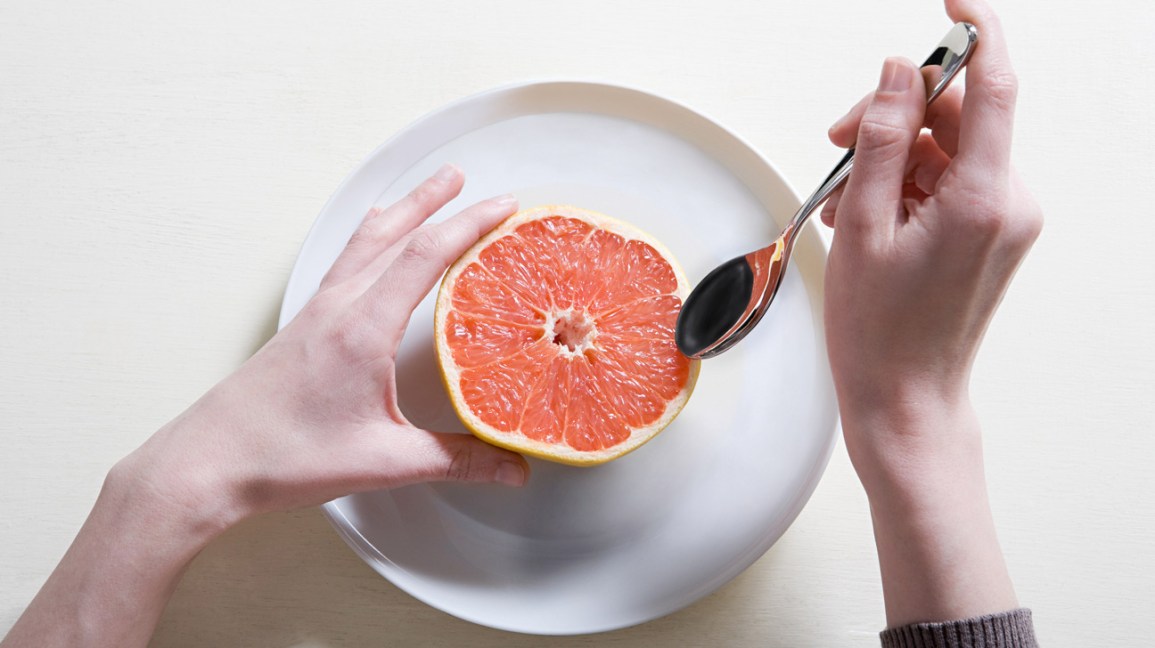 person scooping grapefruit with a spoon