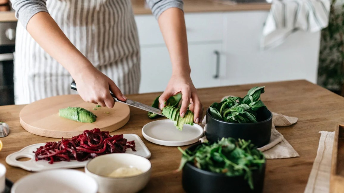 Person moving sliced avocado on a knife from a cutting board to a plate.