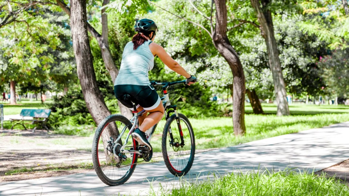 A woman rides a bicycle along a biking trail in a park. 