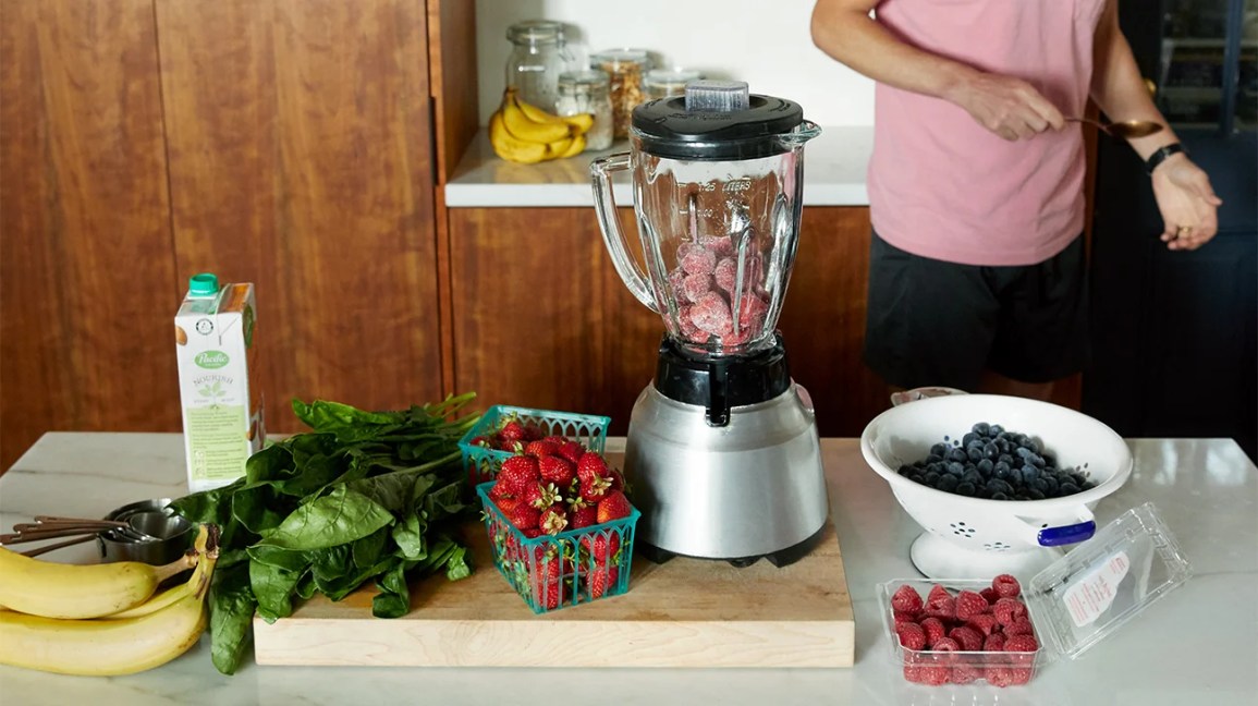 bananas, spinach and berries on a counter with a blender