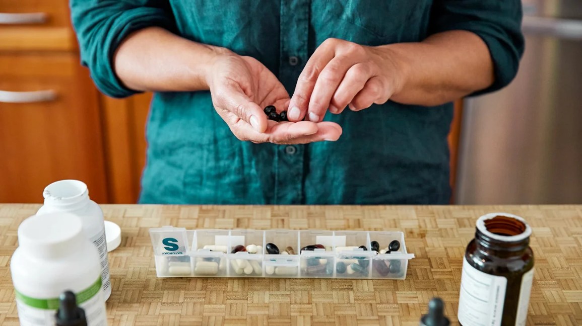 a pair of hands counts out supplements to go in their vitamin case for the week