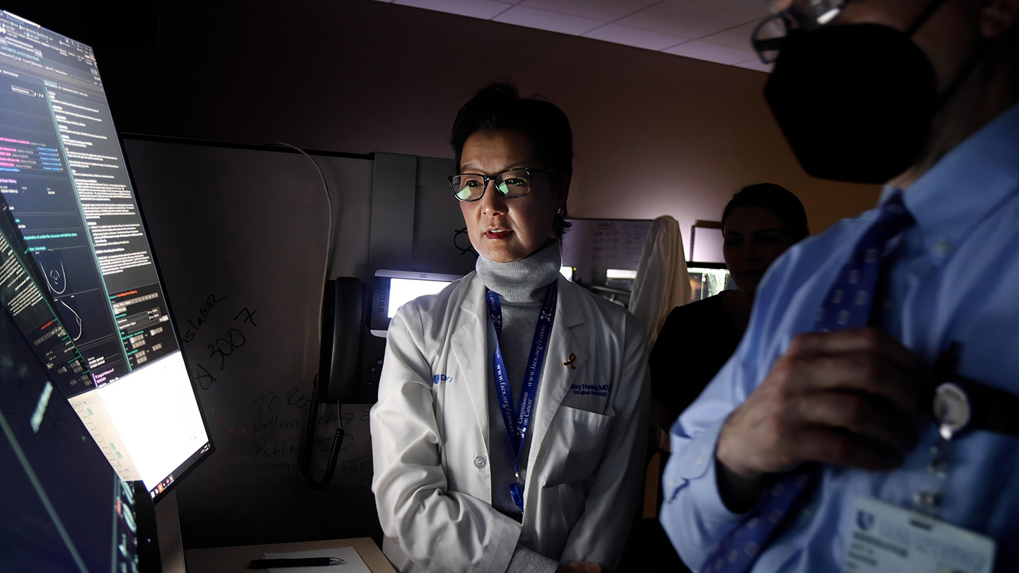 Shelley Hwang wears a lab coat. Her face is illuminated by light from a computer screen where she reviews results from breast cancer testing.