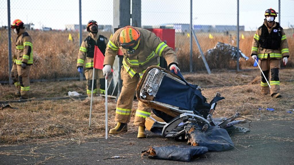 An investigator in a hi-vis outfit picks up the remnants of a plane seat, as others walk behind him