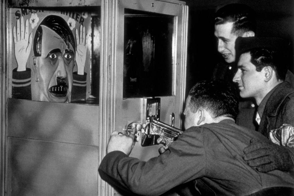 A black and white photo of American soldiers taking pot shots at a caricature of Adolf Hitler, in an amusement arcade set up for them at the Red Cross Club, known as Rainbow Corner, at Piccadilly Circus, London