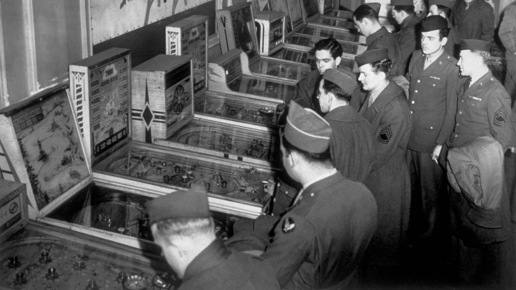 A black and white photo of American soldiers playing pin-ball at Rainbow Corner, the American Red Cross Club for American troops in London