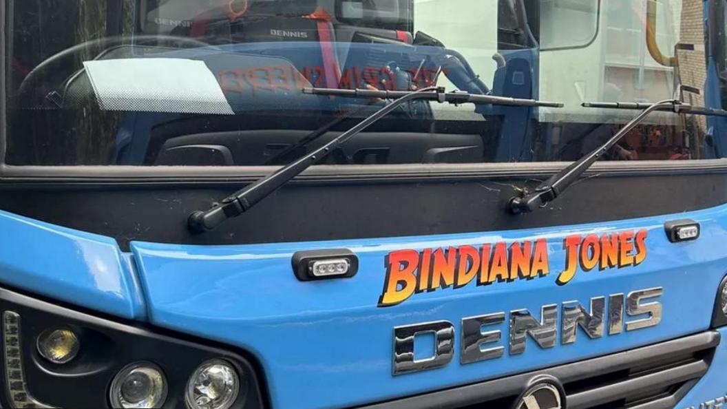 The front of a blue bin lorry with "Bindiana Jones" written in bright yellow to red ombre lettering in the font of the Indiana Jones movies 