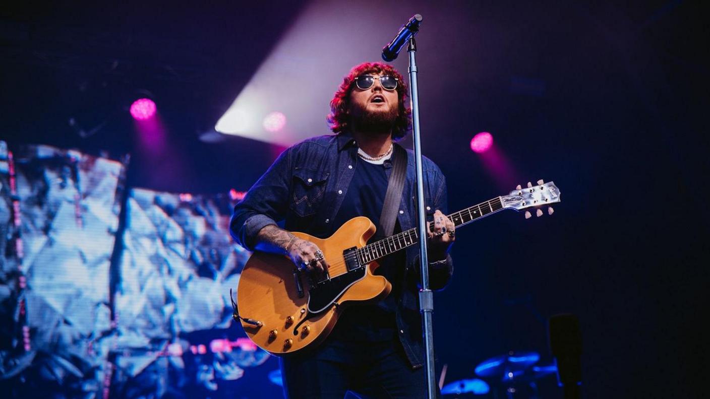 James Arthur performs at Bristol Sounds 2024. He is wearing dark glasses and playing a brown electric guitar.