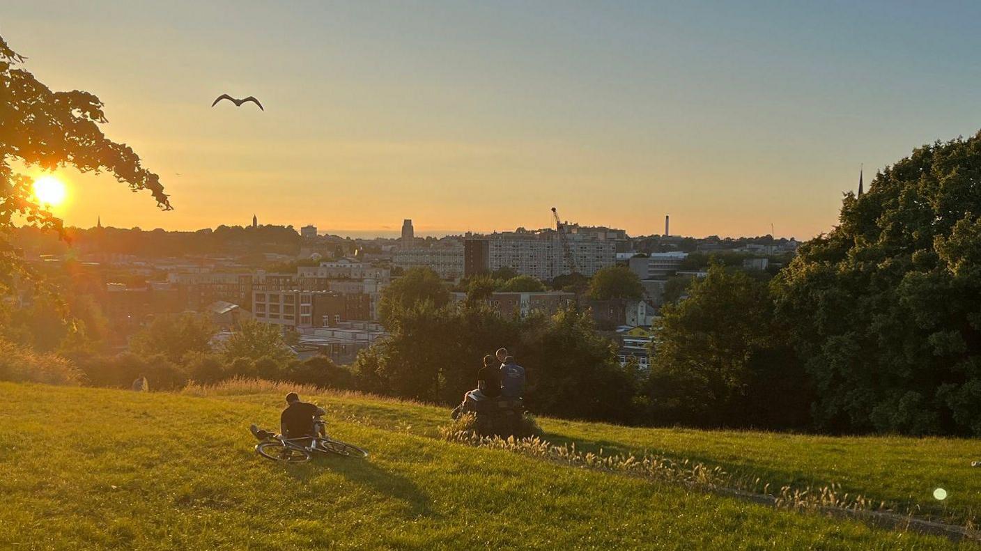 People watch the sun set from Victoria Park in Bristol. Bristol city centre is visible in the background.