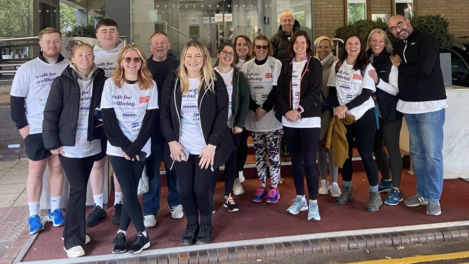 A group of hotel staff from businesses across Bristol and Bath pose for the camera before they set off on a charity walk. Many of them are wearing white T-shirts with the logo of the charity on them and they are mostly smiling