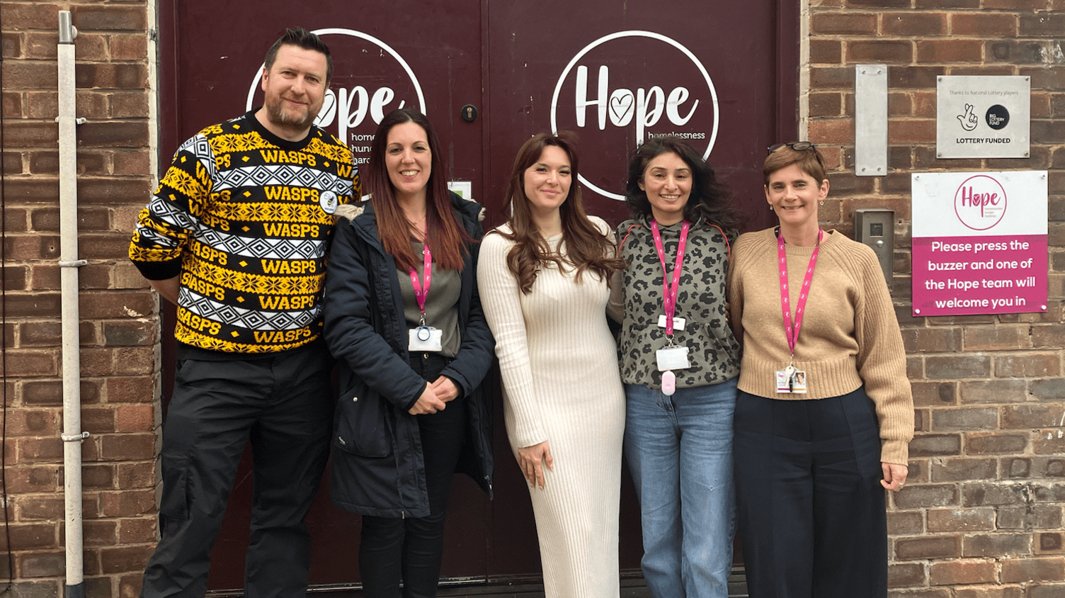 Five people wearing pink lanyards standing outside the Northampton Hope Centre for a group photo.