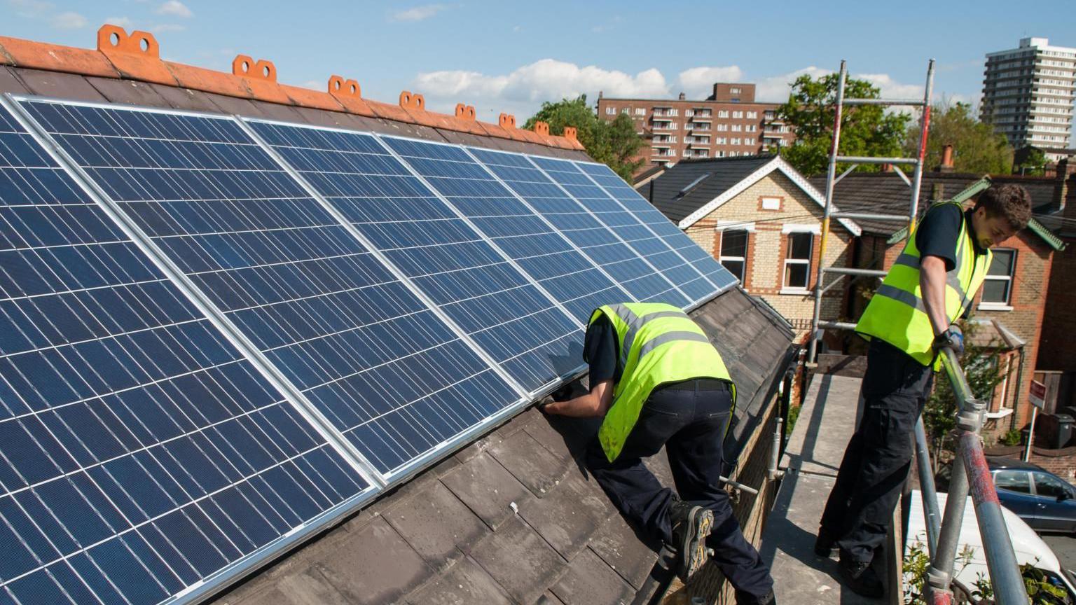 Two men install solar panels on the roof of a house