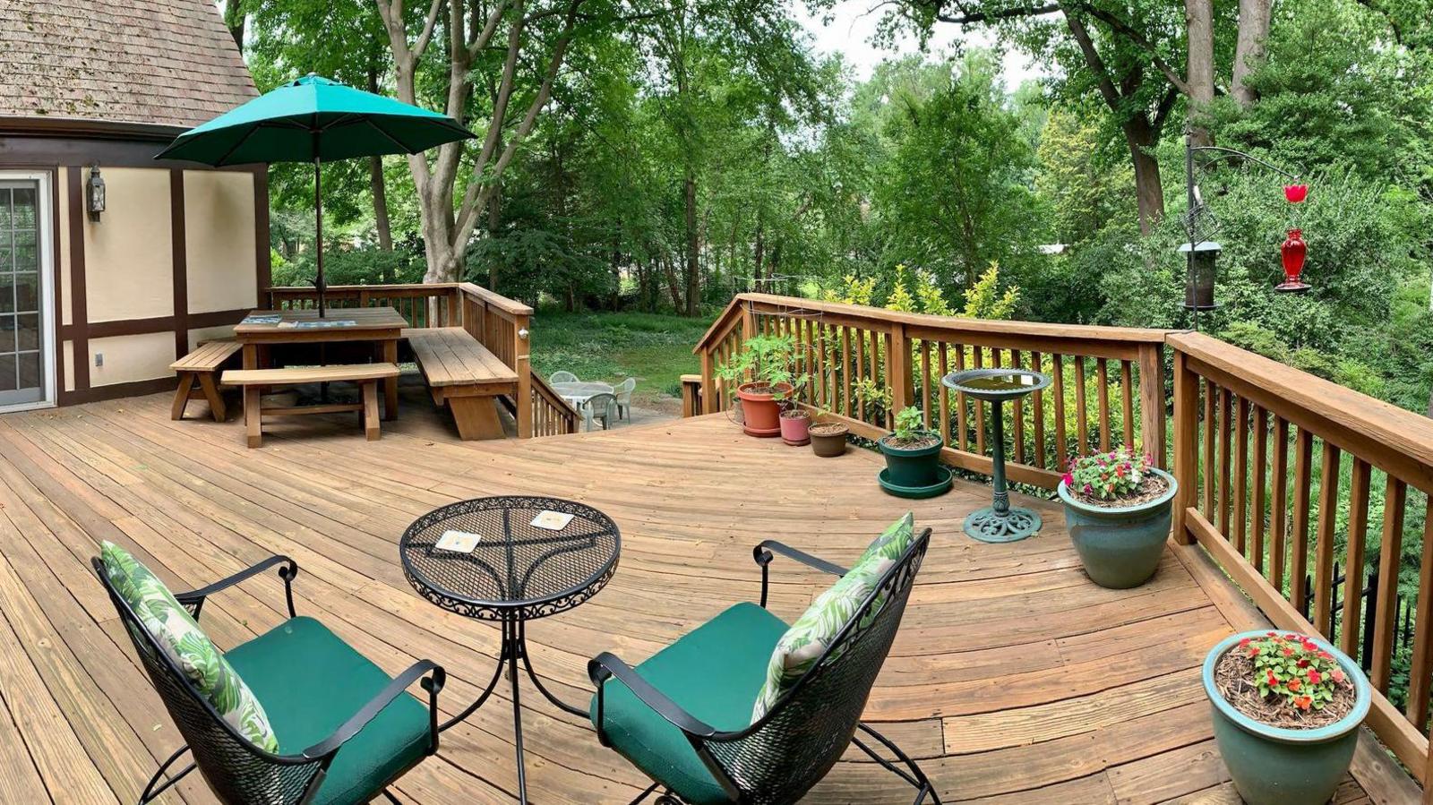 A photograph of the deck shows two chairs in front of a small, metal table. A bigger table and wooden seating is located on the left under a green umbrella. Stairs lead down into the garden.