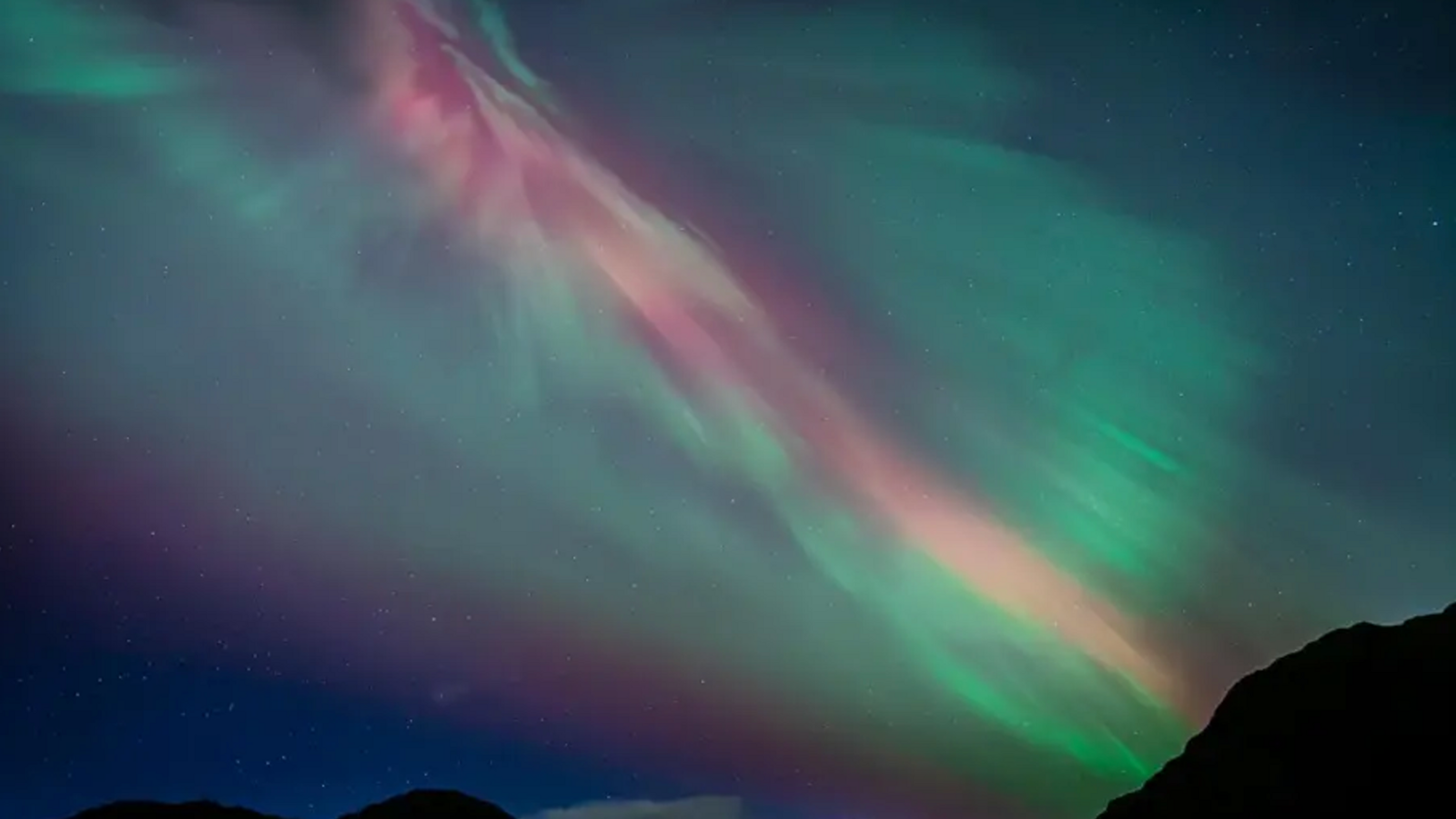 Sky filled with mostly shimmering greens and a streak of red of the aurora