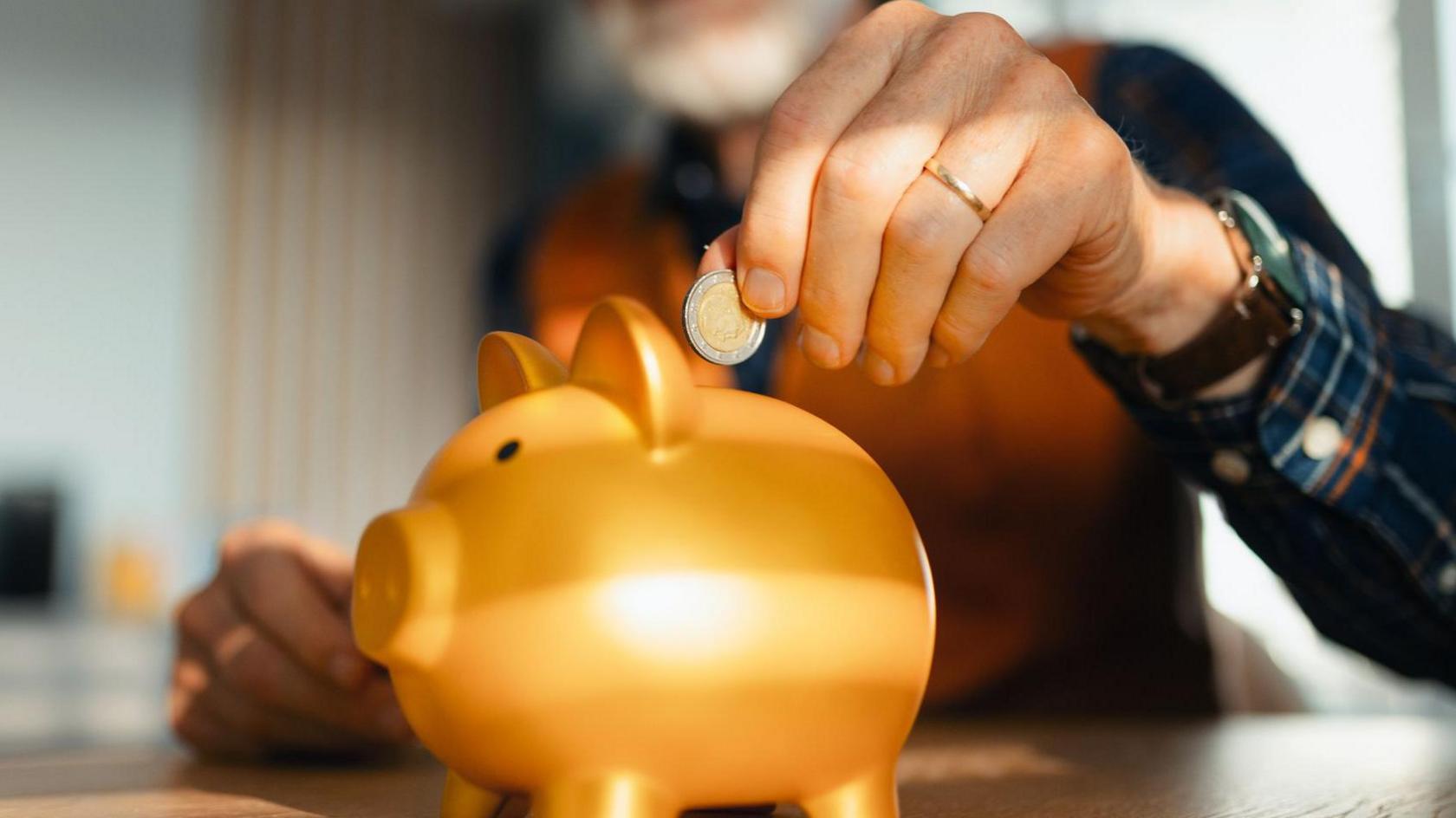 Man placing euro coin into a golden piggy bank 