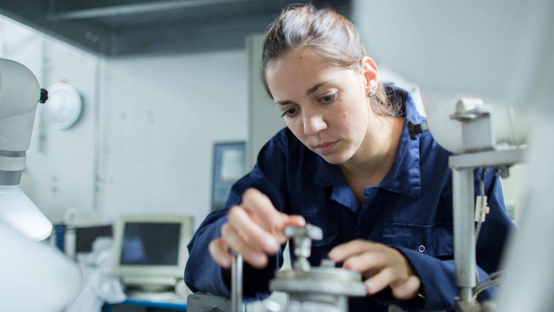 Woman with hair tied back in blue overalls working in a laboratory