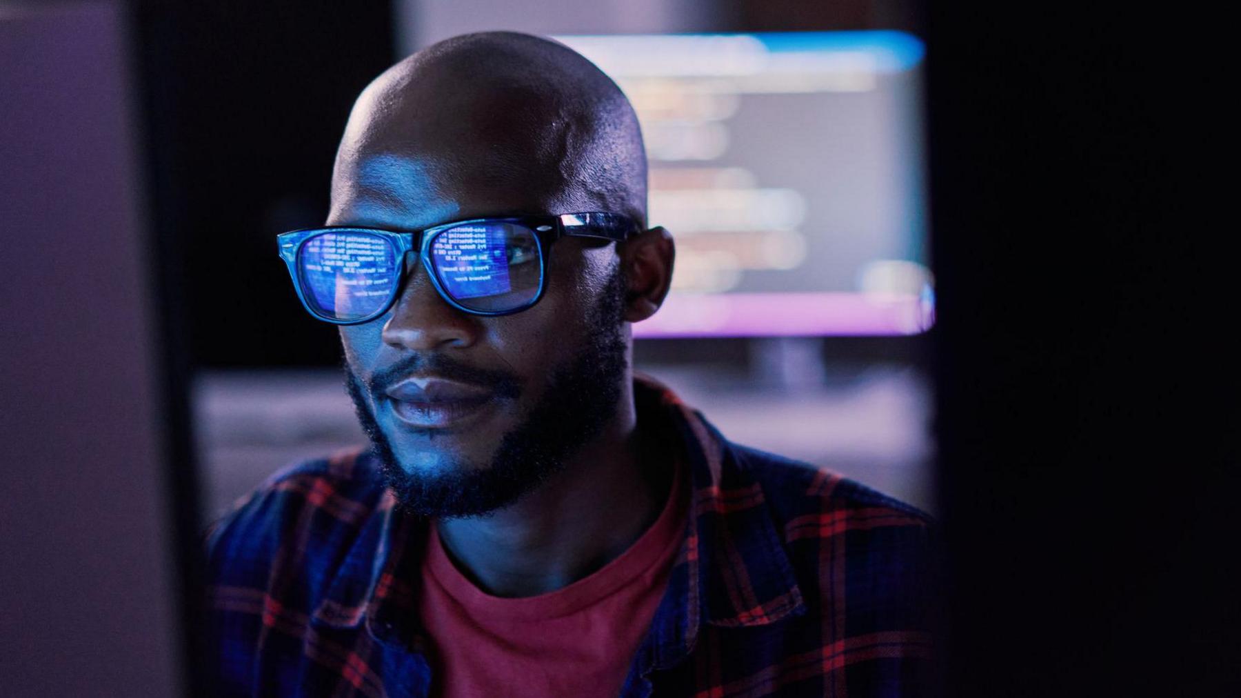 A man looking at a computer screen, which is reflected in his glasses 