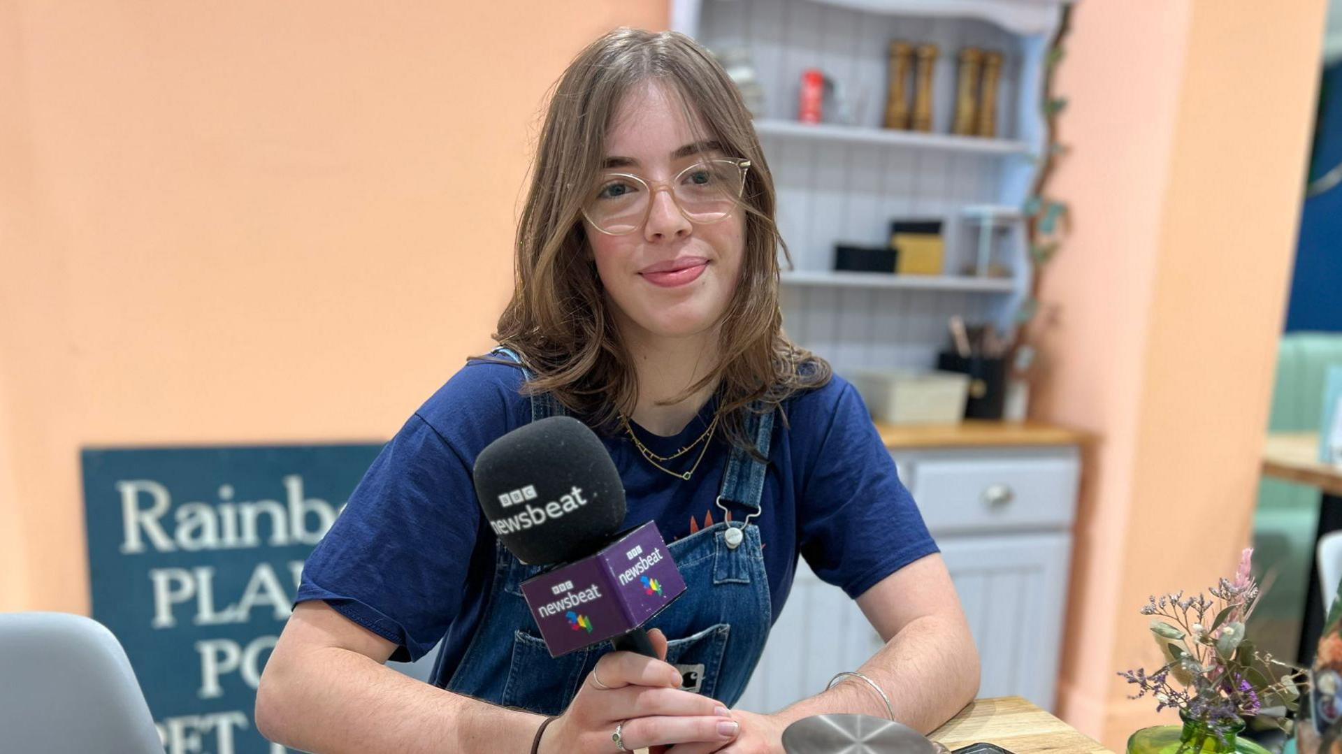 Penelope, a female wearing glasses, holding a microphone while sitting at a table