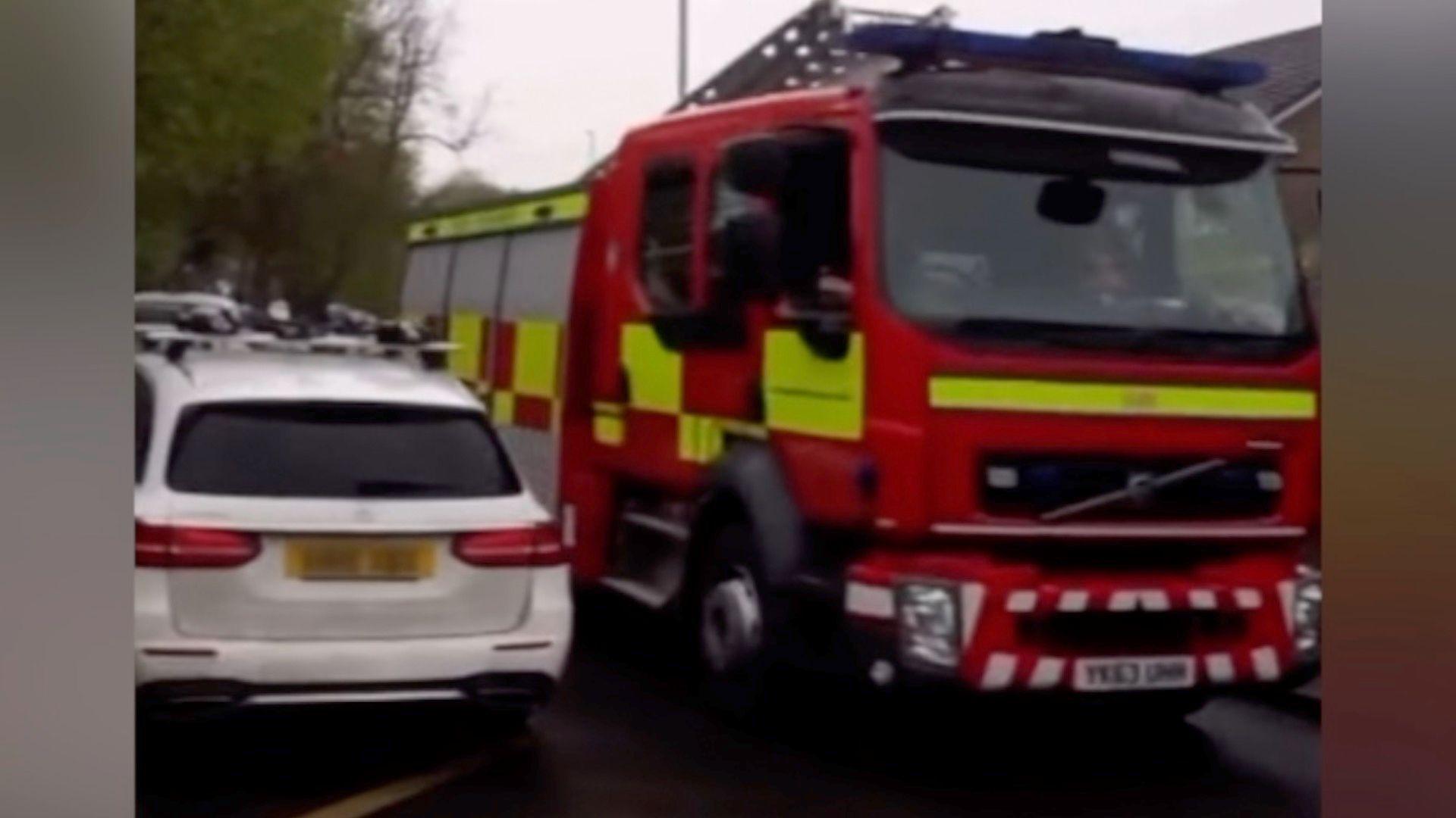 A fire engine driving close to a parked car