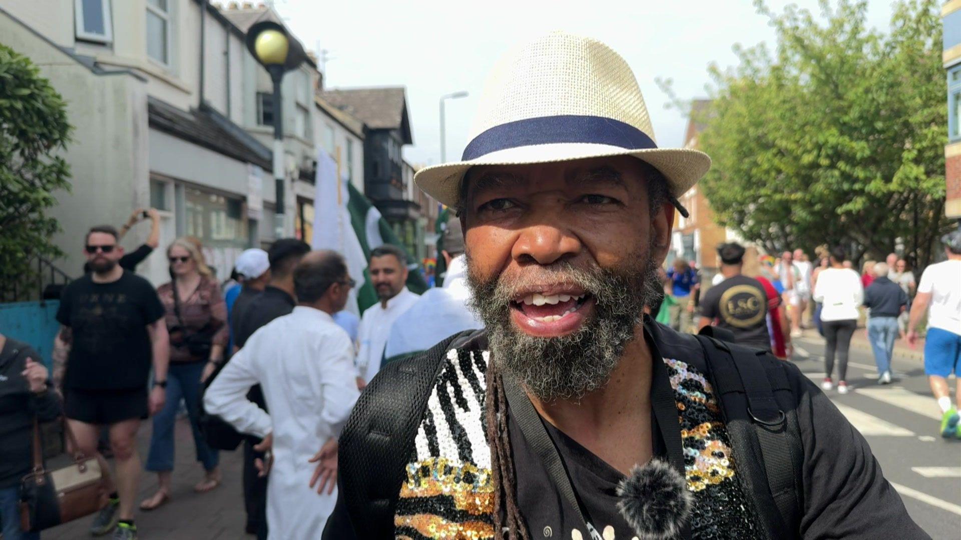 Pax Nindi, who wears a light-coloured hat and a black, beaded top, stands in the street among the crowd at the carnival.