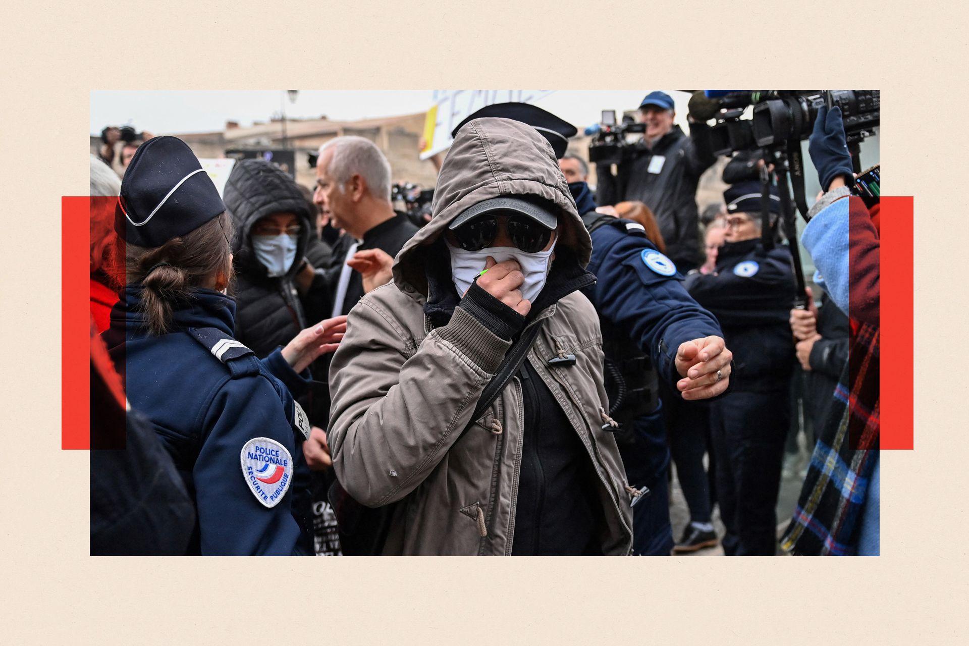 A defendant in a mask walks through a crowd of journalists