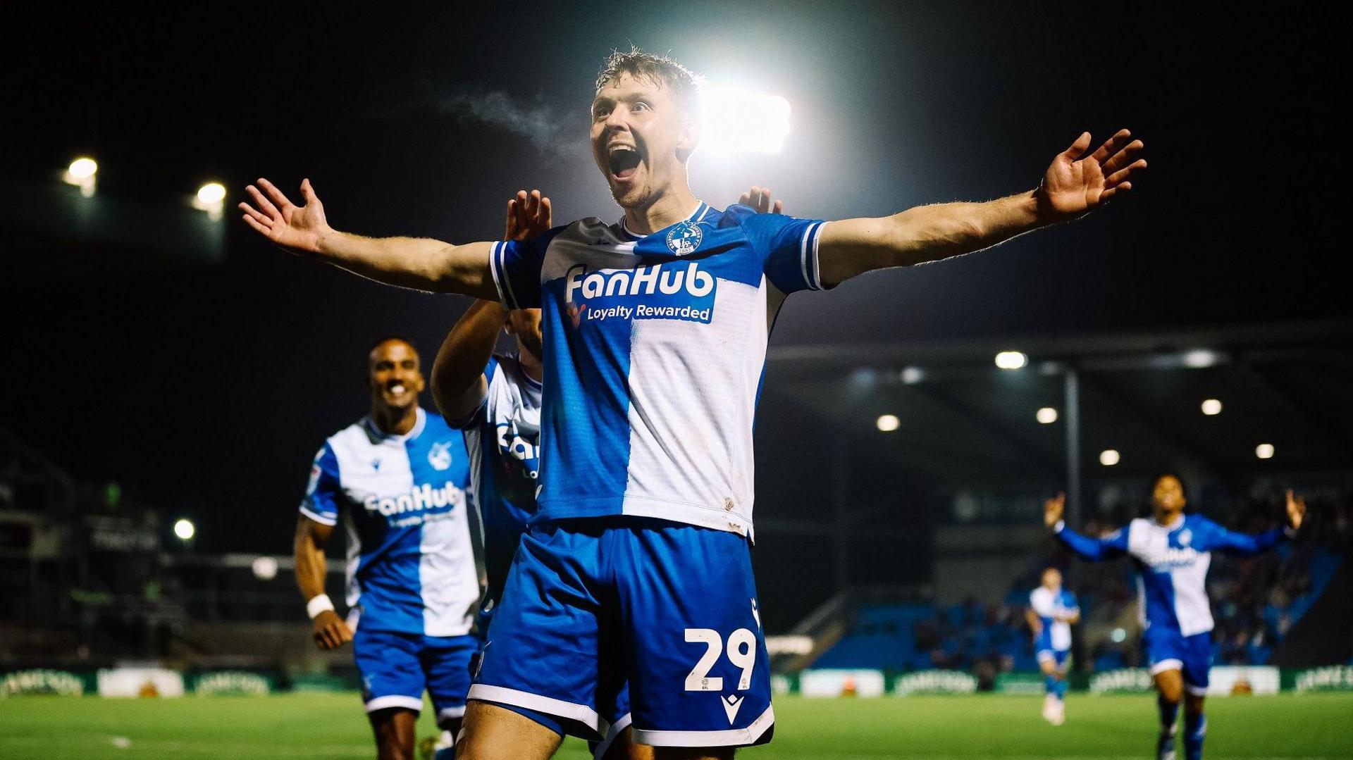 Jamie Lindsay smiles at the fans with his arms wide as he celebrates scoring the only goal of the game as Bristol Rovers beat Shrewsbury 1-0 at the Memorial Stadium. Other Rovers players are running to join in the celebrations.