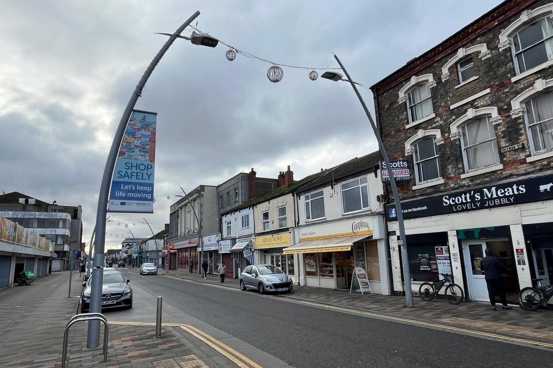 A view of Freeman Street in Grimsby. Shops such as a butcher's and a bakery can be seen beneath a grey sky