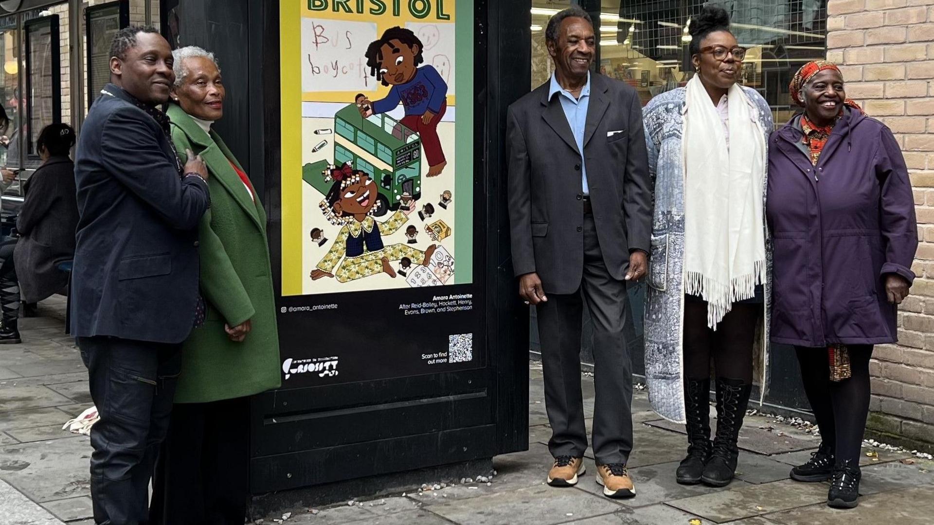 A group of pioneers from the Bristol Bus Boycott smile at the camera as they stand next to new artwork on a bus stop near The Lanes in Bristol city centre