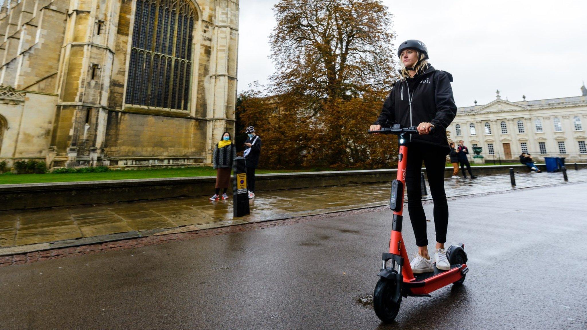 Woman riding past King's College Chapel in Cambridge on e-scooter