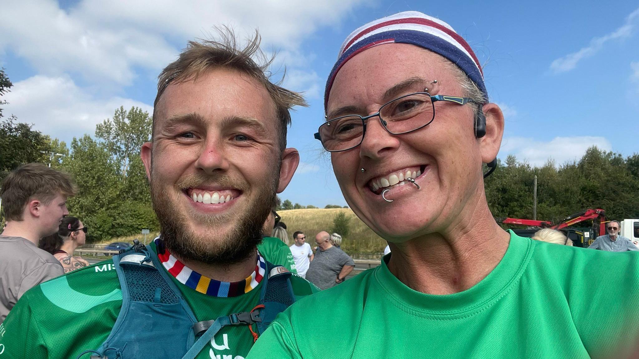 If U Care Share founder Matthew Smith and Nikki Gaynor are smiling widely for a selfie. They are both wearing green 'if u care share' sports tops.