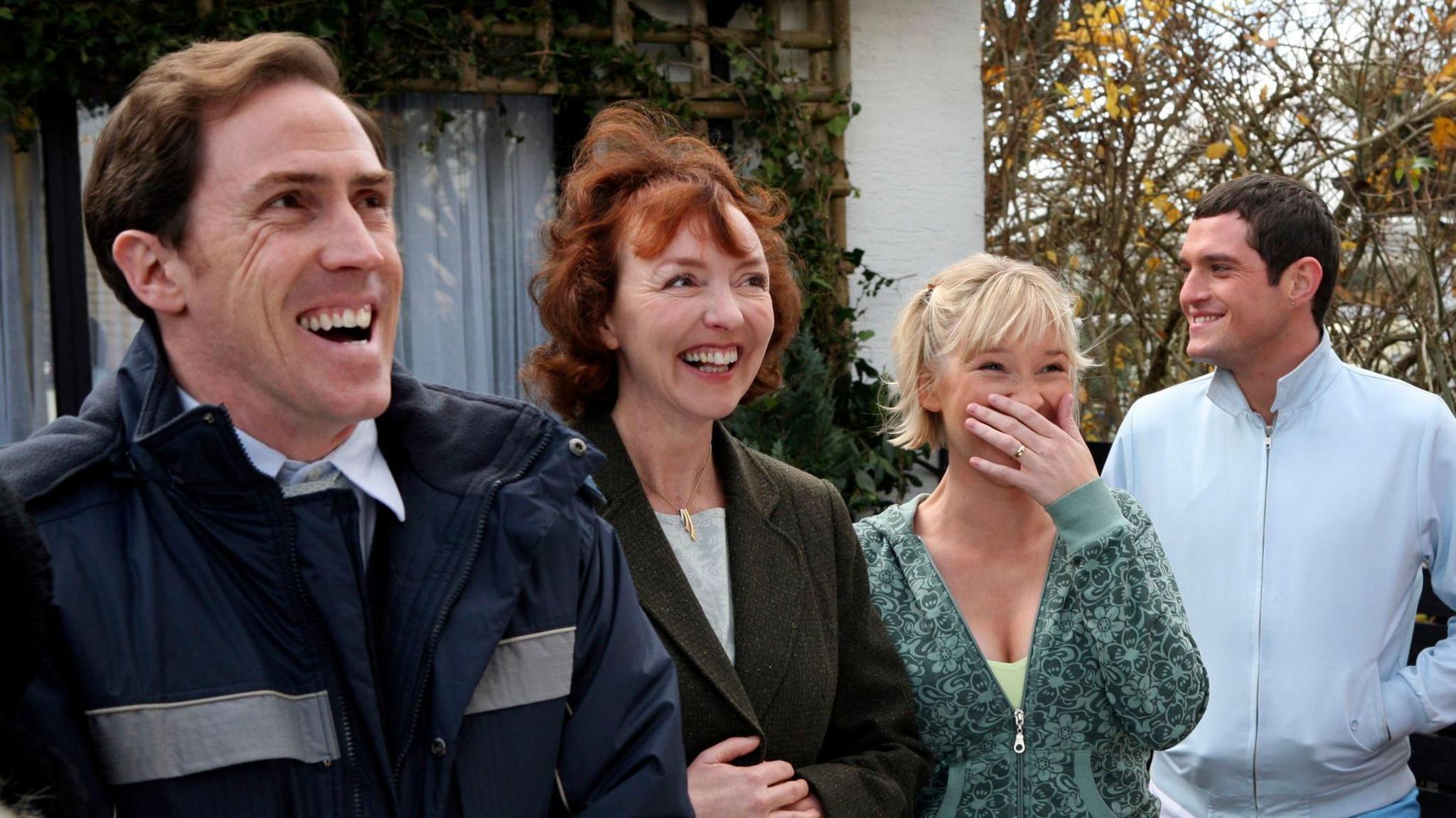 Four members of the Gavin and Stacey cast standing outside one of the homes where the sitcom was filmed. They are all dressed in winter jackets and are laughing at something just off to the right of the camera. 