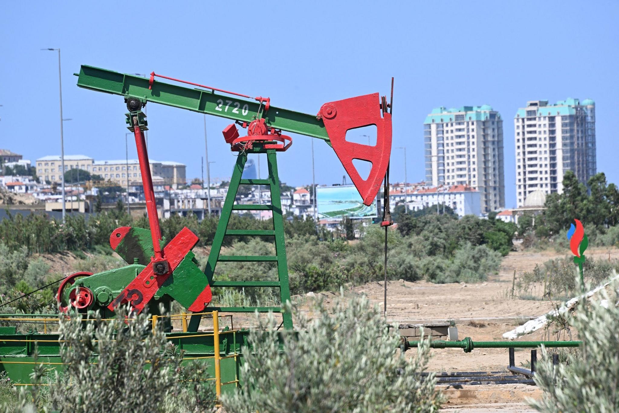 A 'nodding donkey' oil drilling operation with high rise buildings in the background.