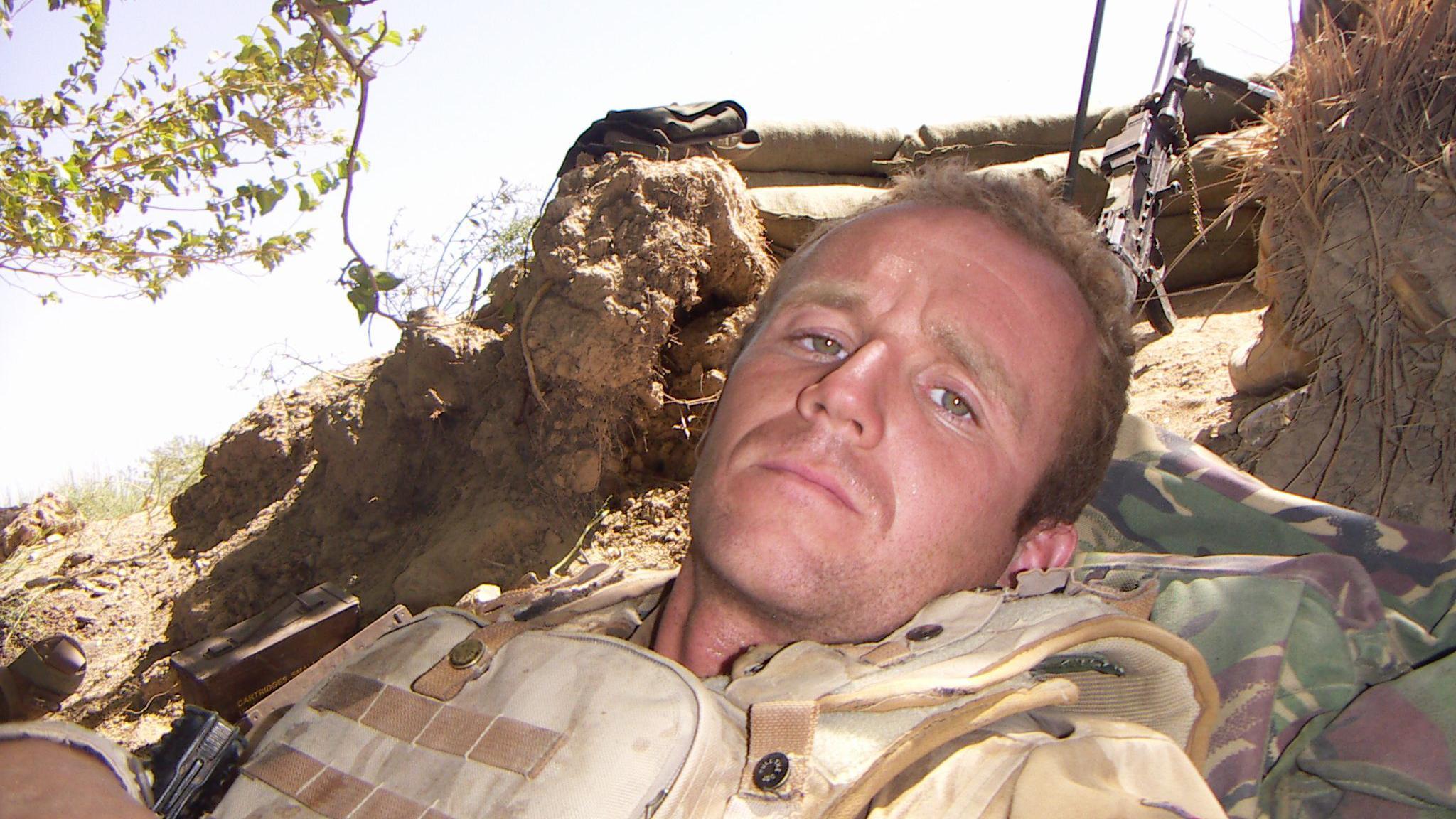 Sgt Peters in Helmand Province in 2009 wearing military uniform with a machine gun in the background