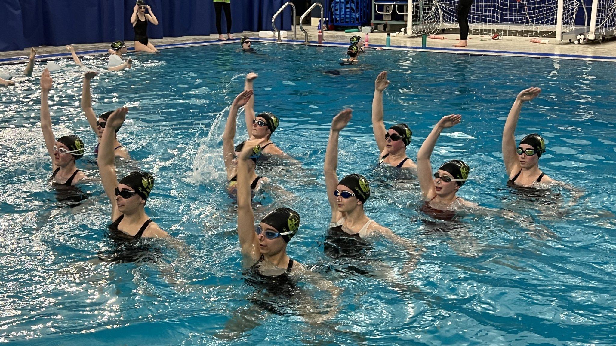 Artistic swimmers performing a routine in a swimming pool