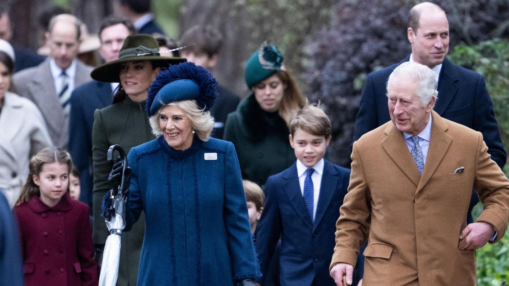 Several members of the Royal Family in winter coats walk together to attend a church service. Queen Camilla and King Charles III lead the family.