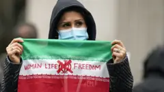 倫敦特拉法加廣場一位女士舉起寫上「女性、生命、自由」字樣的伊朗國旗抗議（29/10/2022）
