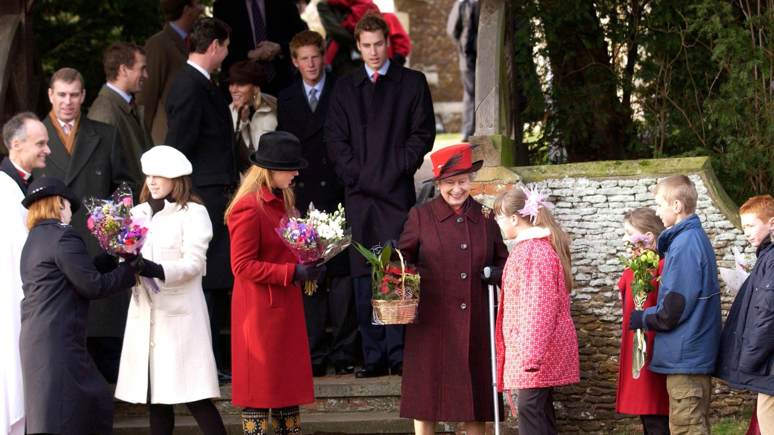 Royals after the traditional Christmas Day service gather on steps of church. Queen Elizabeth II is helped by her granddaughters Princess Beatrice And Princess Eugenie as she receives flowers and gifts from children in the crowd. 