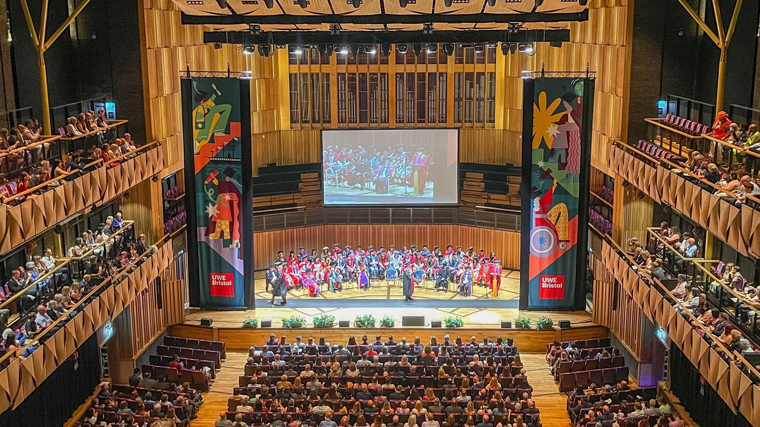 Hundreds of students and their families sit in seats at the Bristol Beacon for a UWE graduation ceremony. The picture is taken from the upper tier of the music venue