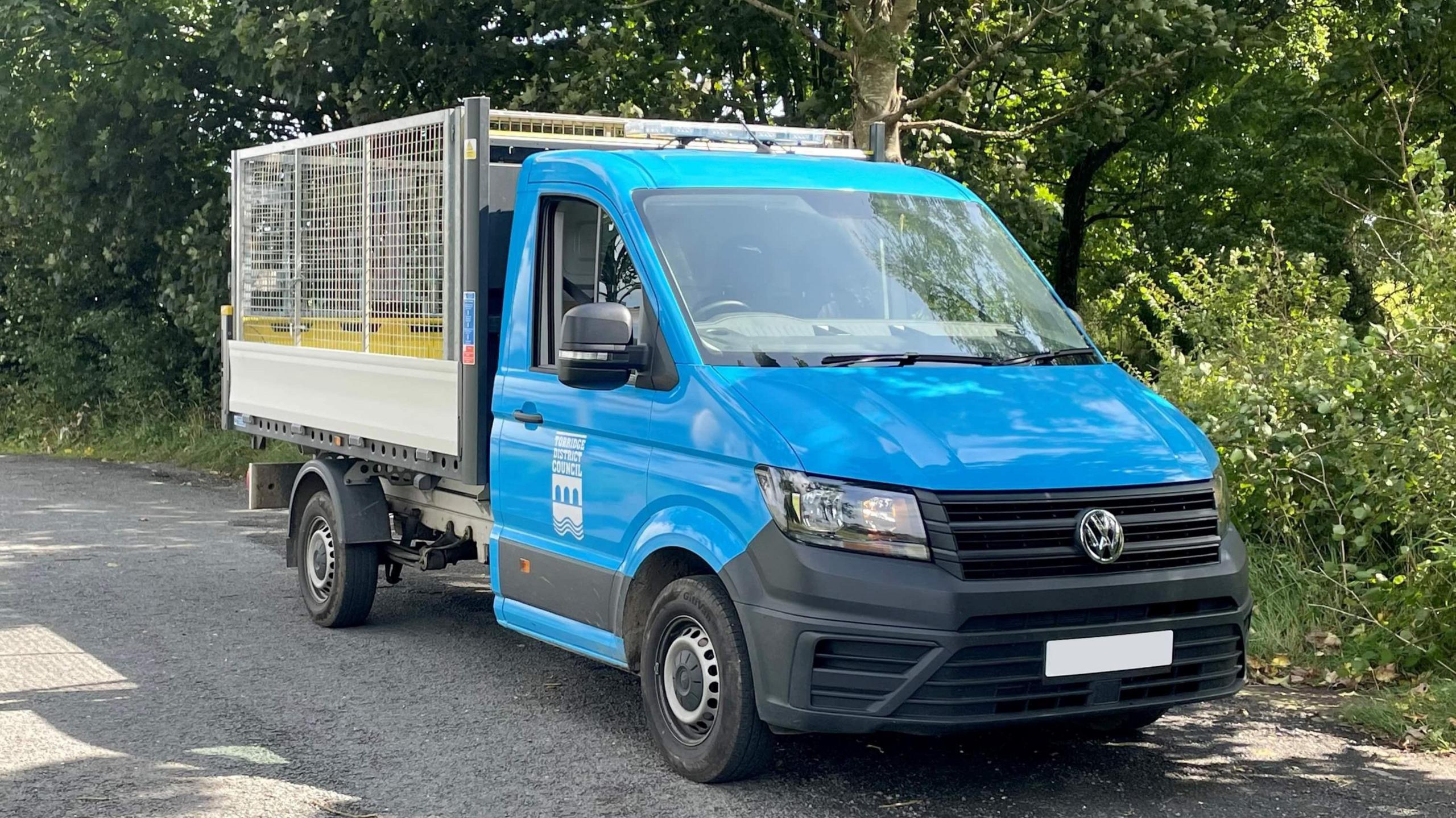 A blue street cleansing van. It has a large cage on the back for securing waste and other items 