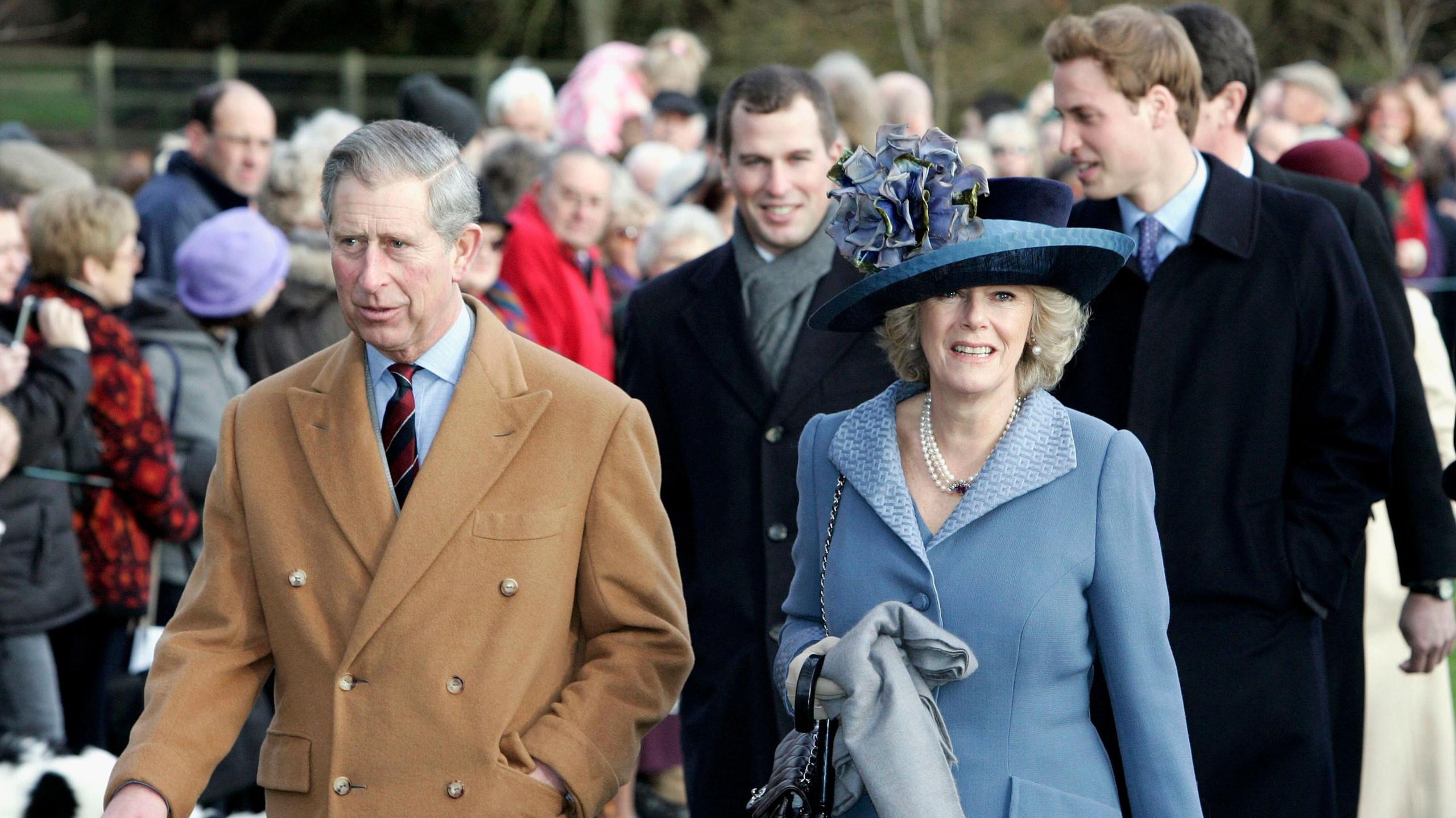 The King and Queen in 2005 walking from church with Prince William and Peter Phillips. King Charles is wearing a camel coloured coat, his wife Queen Camilla is dressed in a mid-blue coat, and matching navy and blue hat. She wears pearls. Prince William and Peter are wearing dark overcoats. Crowds line the walkway.