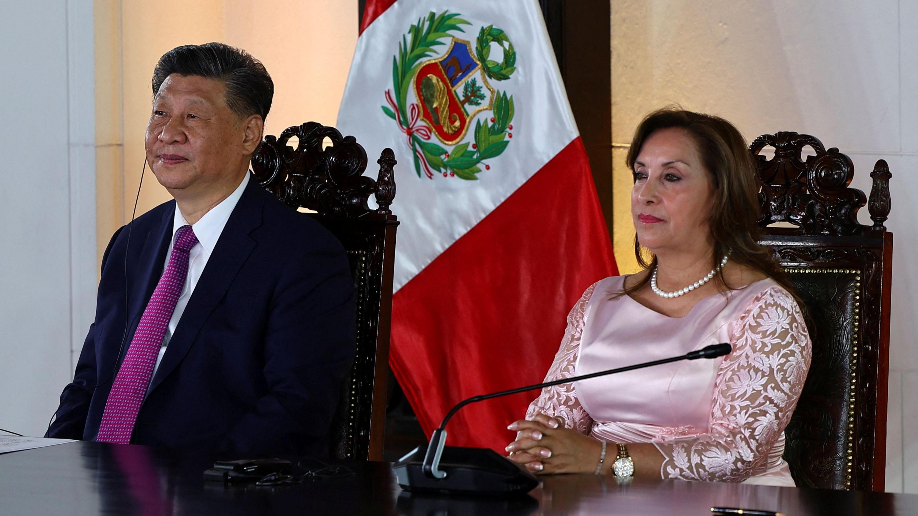 Chinese President Xi Jinping with Peruvian President Dina Boluarte on 14 November. The pair are sitting at a table in front of a Peruvian flag.