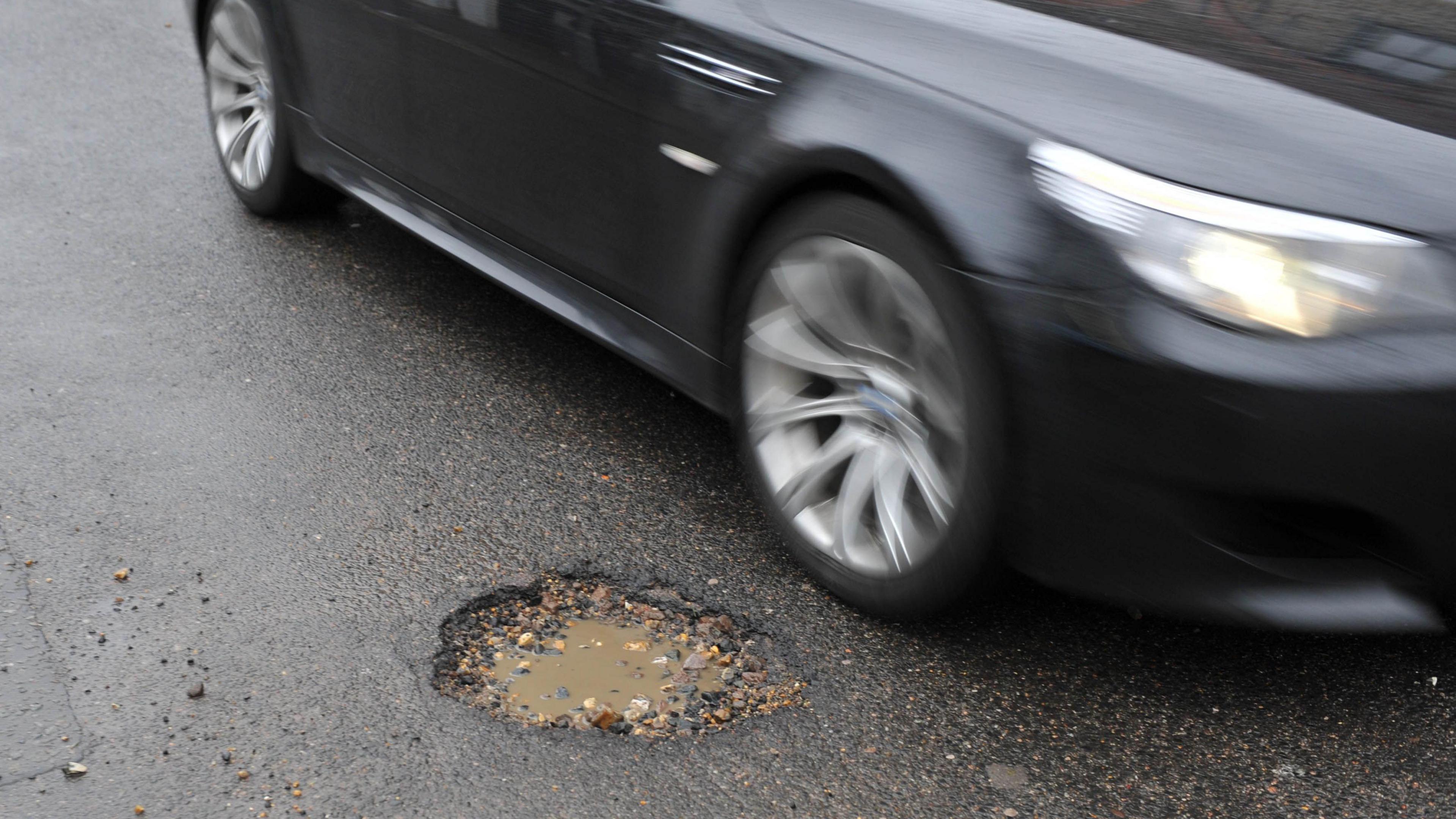 A black car driving by a pothole in the middle of a road