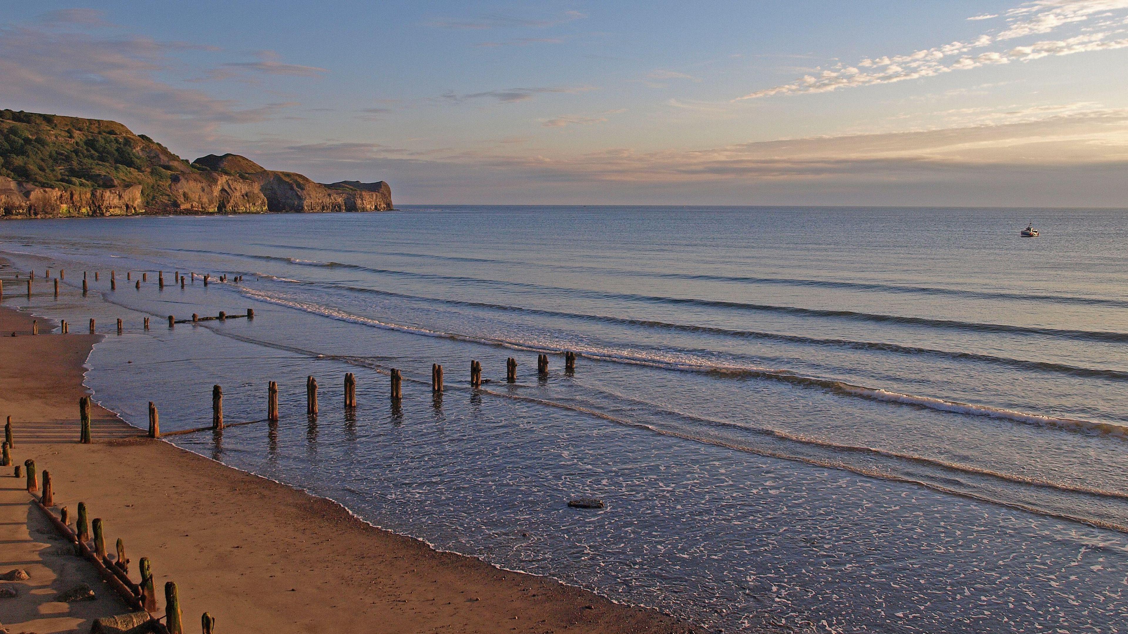 Sandsend beach at sunset, with groynes reaching out into the low tide and a boat in the distance.