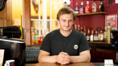 Alex Barry, a young man with blond hair, stands behind an old fashioned bar in a pub.