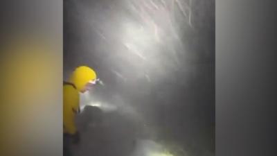 A darkened nighttime image with a rescuer wearing a yellow-hooded jacket while snow pelts in the background